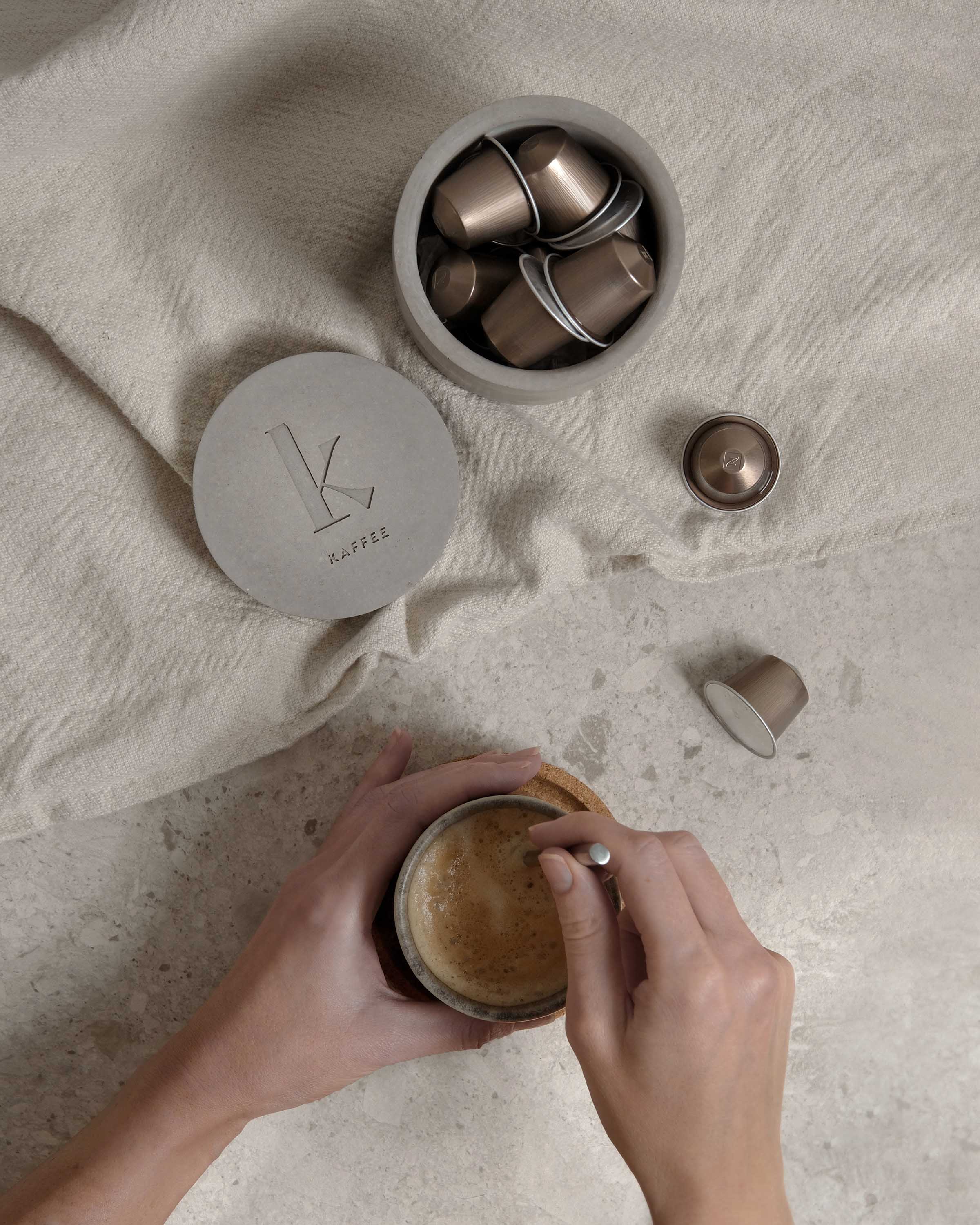 Concrete lid with a custom debossed logo next to matching concrete container and a person holding a coffee cup.